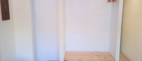A walk-in closet with a wooden bench, a hanging rod, and a small storage box.