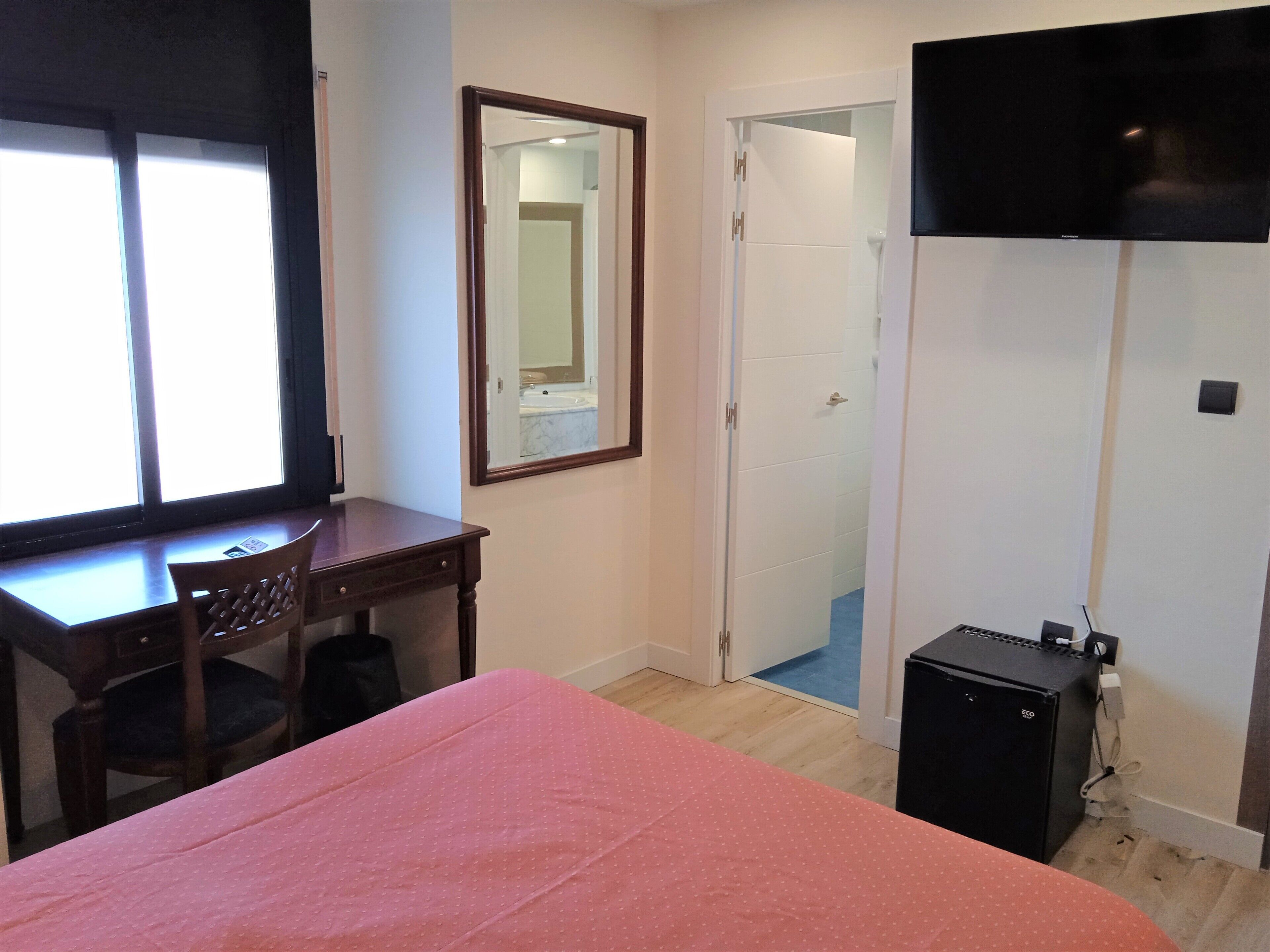 A bedroom with a bed, a desk, a chair, a TV, and a wardrobe.