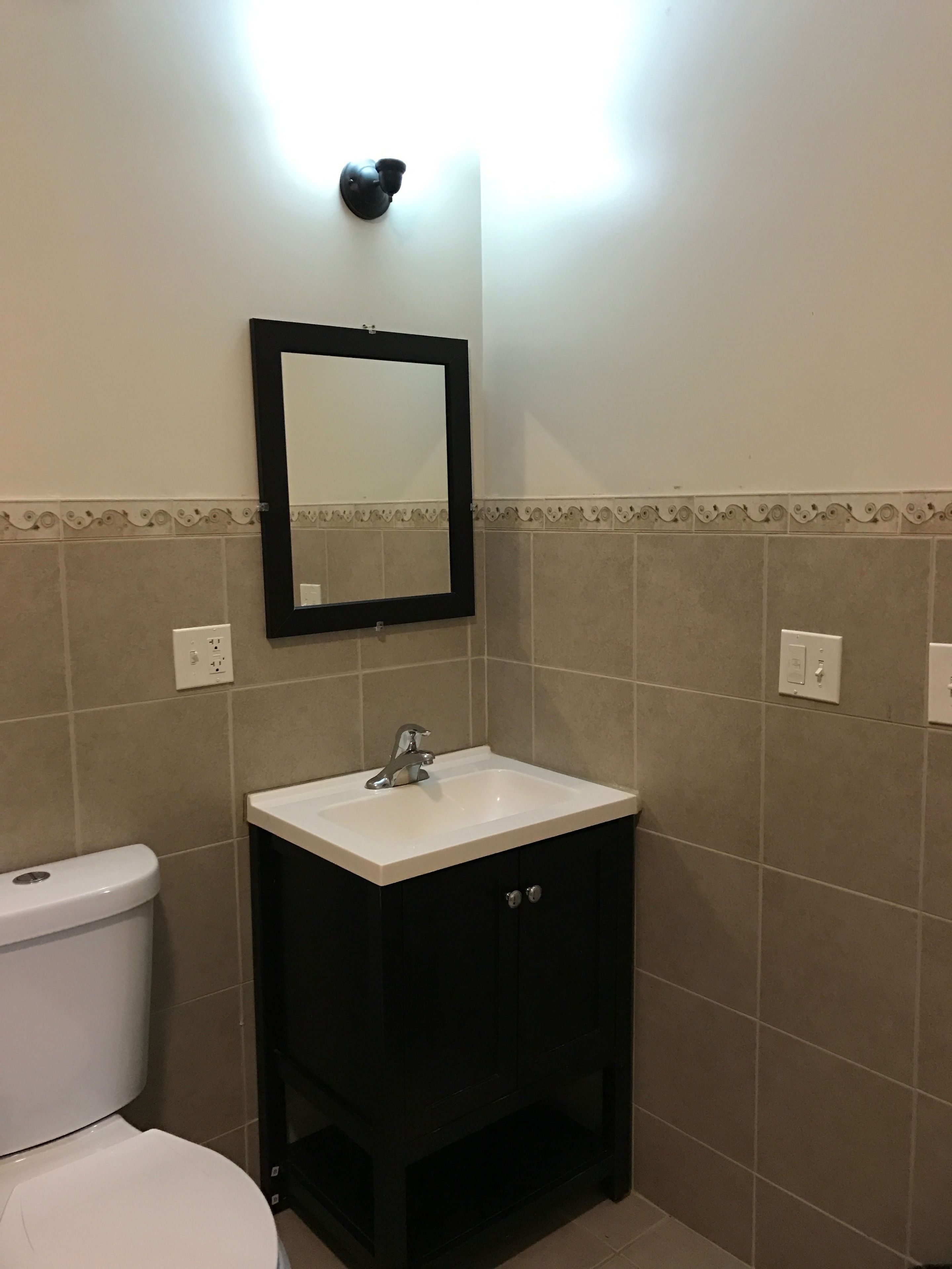 Un baño con un lavamanos blanco, un gabinete negro y un espejo encima.