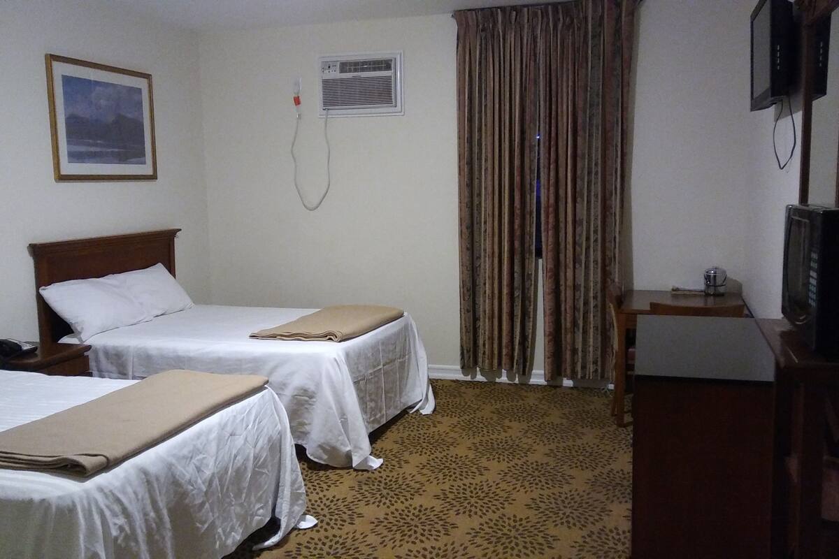 A hotel room with two beds, a television, an air conditioning unit, and a patterned carpet.