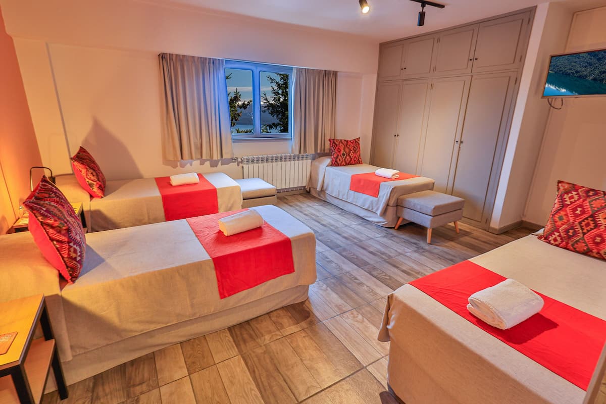 A hotel room with two single beds, a sofa, a TV, and a window with curtains.