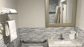 A compact bathroom with a white toilet, a sink with a marble countertop, a mirror with a diamond pattern, and a towel rack with white towels. - Executive Suites Inn (Westminster)