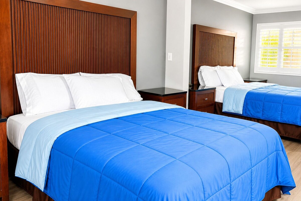 A hotel room with two beds, wooden headboards, and a window with blinds.