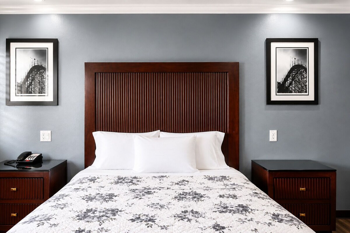 A hotel room with a large bed, two bedside tables, a wooden headboard, and two framed pictures on the walls.