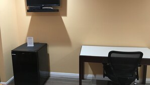 A hotel room with a desk, a chair, a television mounted on the wall, and a small black refrigerator. - Executive Suites Inn (Westminster)