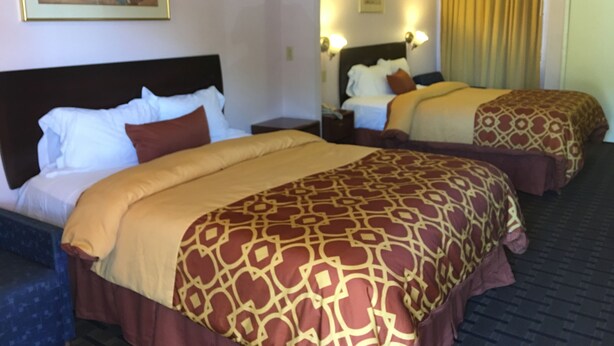A hotel room with two beds, a large painting on the wall, and a mirror reflecting the room. - Executive Suites Inn (Westminster)