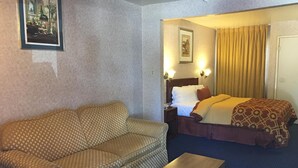 A hotel room with a sofa, a bed, a nightstand, and a small table. - Executive Suites Inn (Westminster)