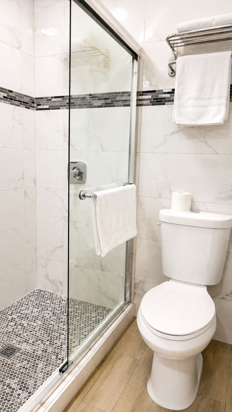 Un baño con ducha cubierta por vidrio, inodoro y suelo de baldosas.