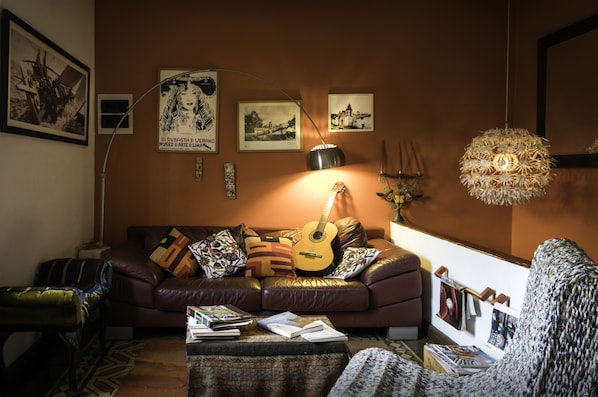A cozy living room with a leather sofa, a guitar, and various framed pictures on the wall.