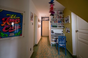 A narrow hallway with a tiled floor, a bookshelf, a desk, and a chair.