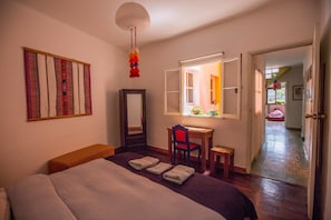 A bedroom with a bed, a desk, a chair, a mirror, and a window.