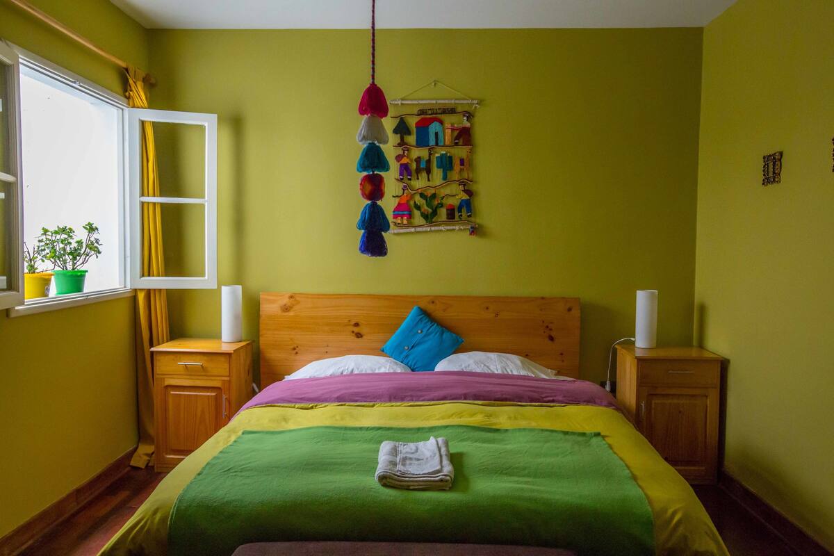 Una habitación con una cama, una ventana, un cuadro en la pared y un mueble pequeño.