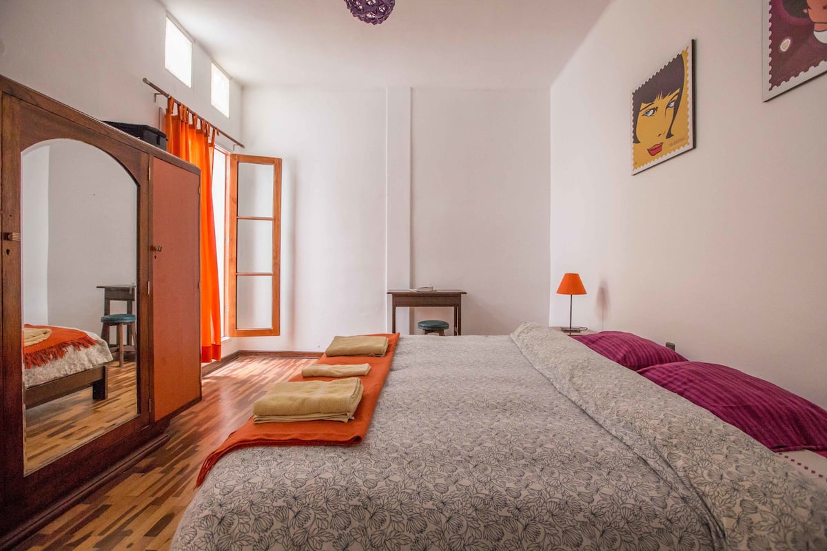 Un dormitorio con una cama, un armario de madera, un espejo, un escritorio y una lámpara.