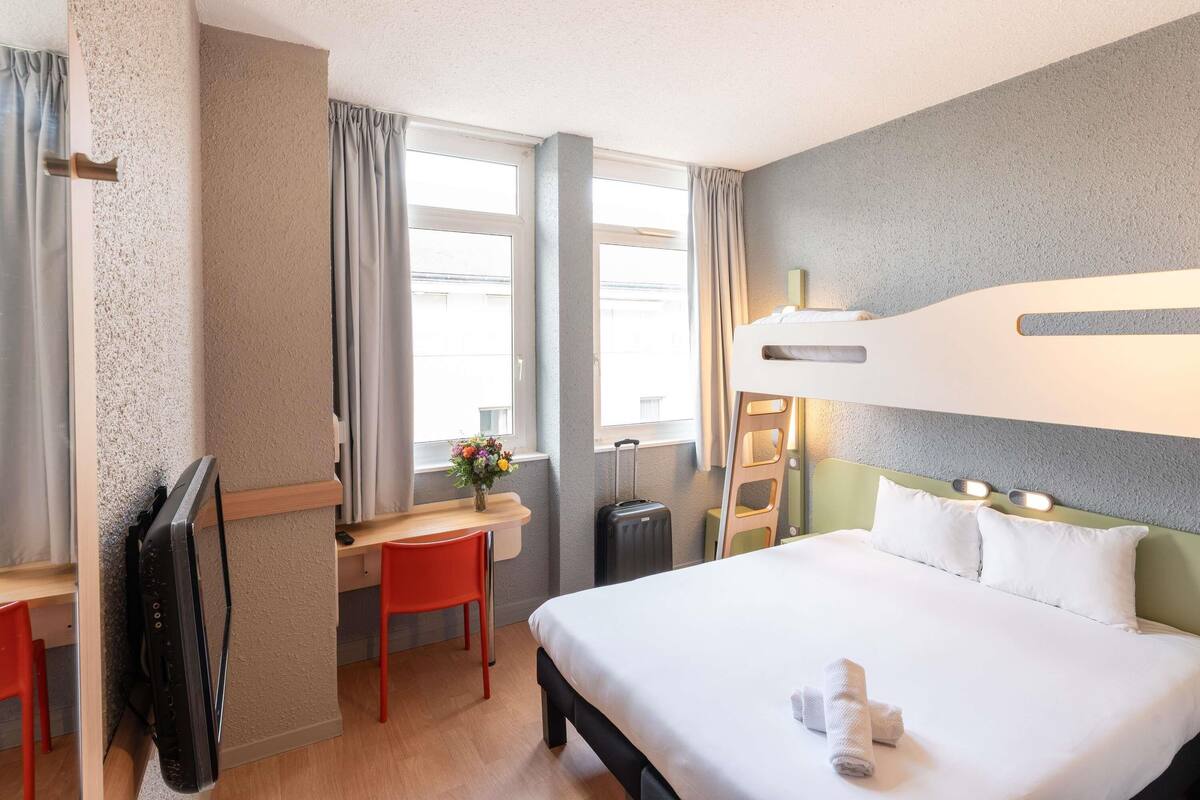 A hotel room with a bed, desk, chair, and a window with curtains.