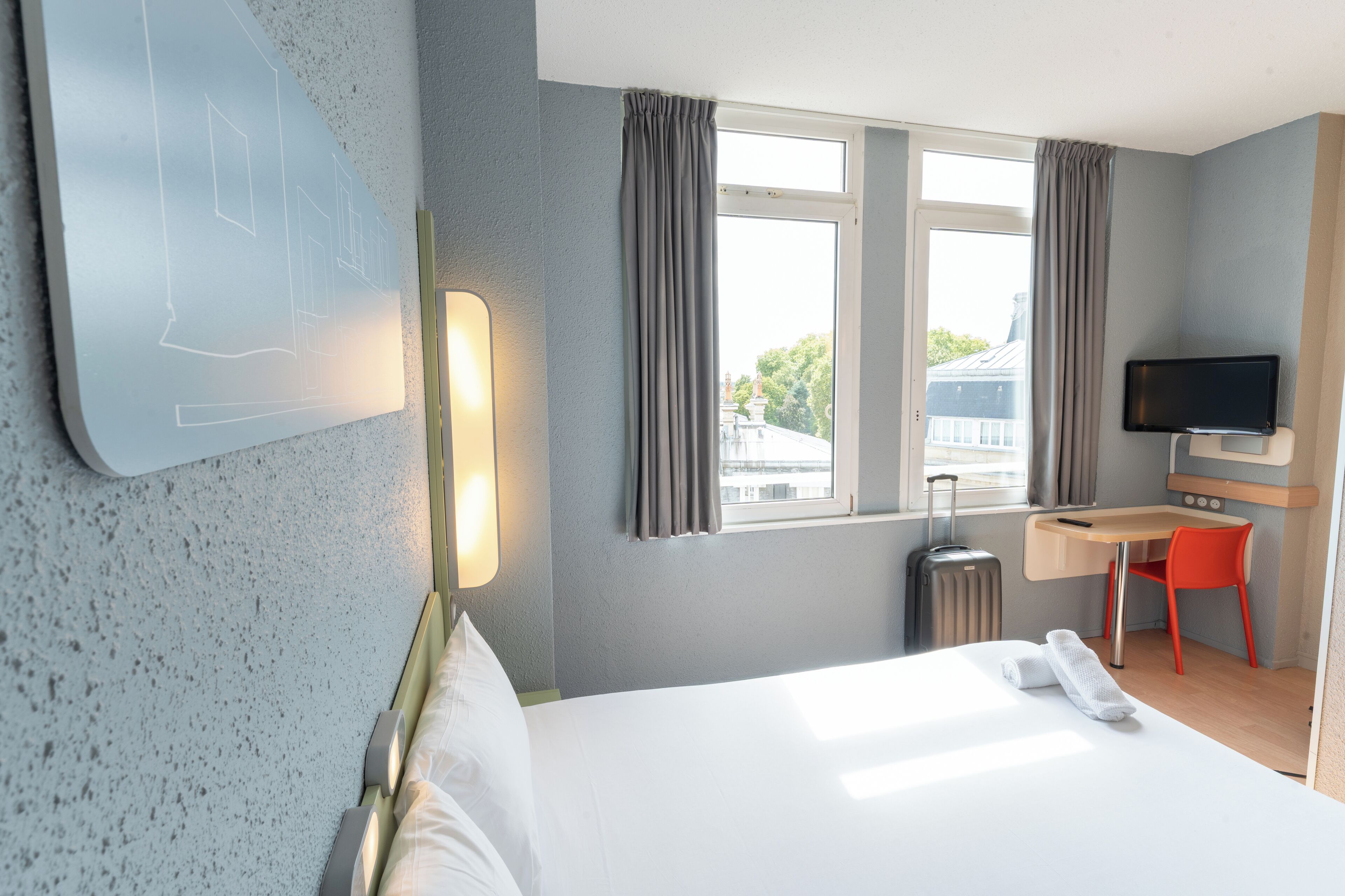 A hotel room with a bed, a desk, a TV, and a window with curtains.