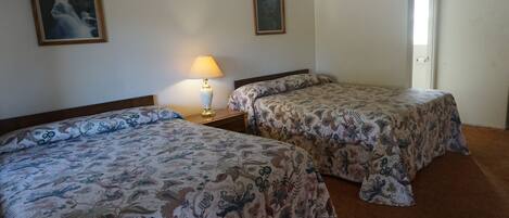 A hotel room with two beds, a nightstand with a lamp, and two framed pictures on the wall.
