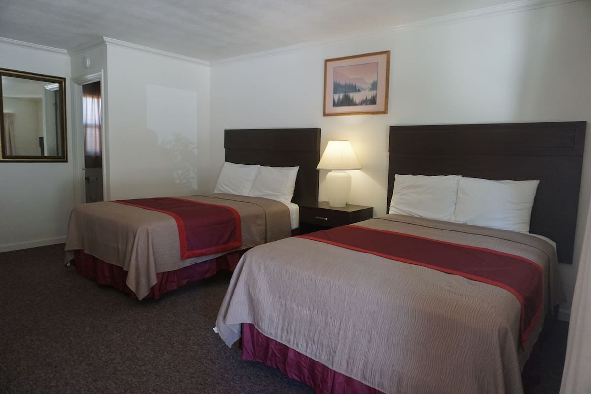 A hotel room with two beds, each with a red and beige bedspread, a nightstand with a lamp, and a framed picture on the wall.