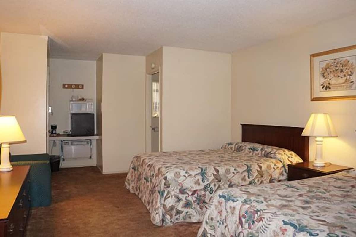 A hotel room with two beds, a desk, a chair, a microwave, and a small kitchenette.