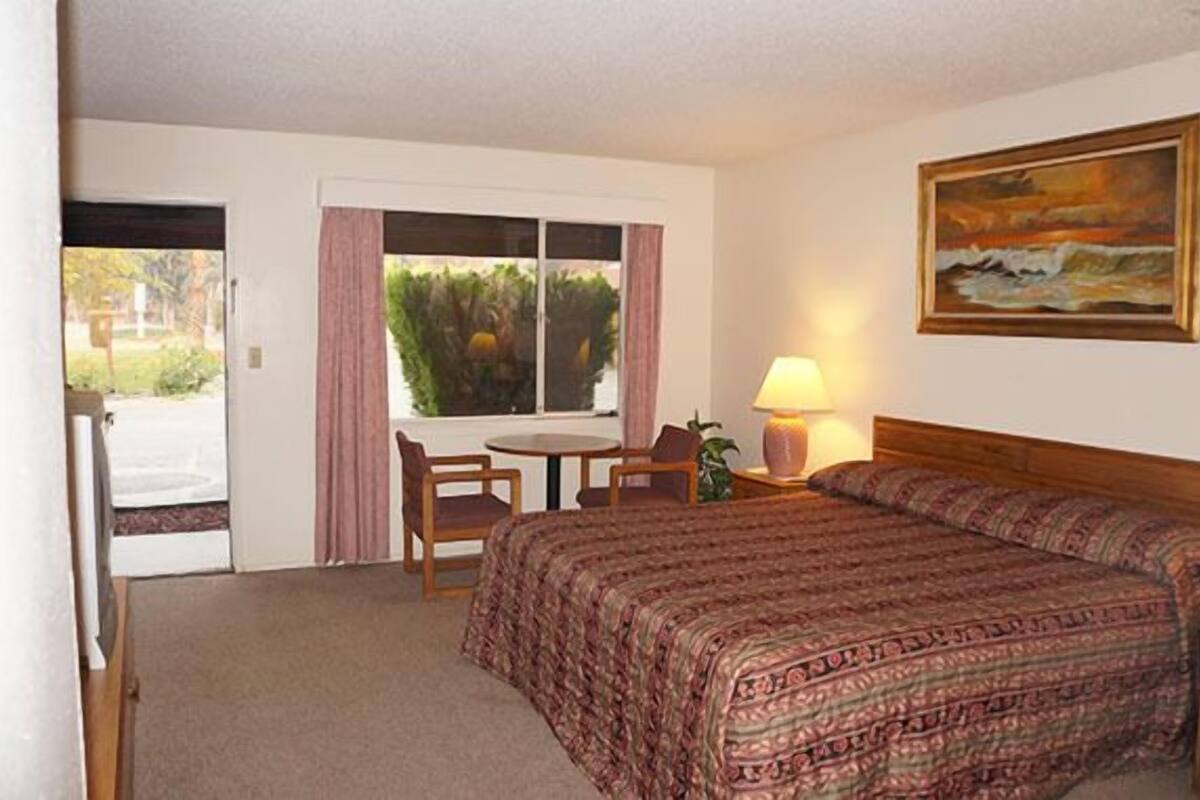 A hotel room with a bed, a desk, a chair, a lamp, and a painting on the wall.