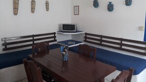 A dining area with a wooden table, chairs, and benches. There is a television on a stand and decorative vases on the wall. - Hotel y Bungalows Los Arcos (San Patricio Melaque)