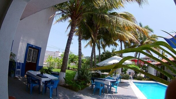 A poolside area with blue chairs and tables, a pool, and palm trees. - Hotel y Bungalows Los Arcos (San Patricio Melaque)