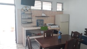 A compact kitchen with a gas stove, a refrigerator, and a dining table with chairs. - Hotel y Bungalows Los Arcos (San Patricio Melaque)