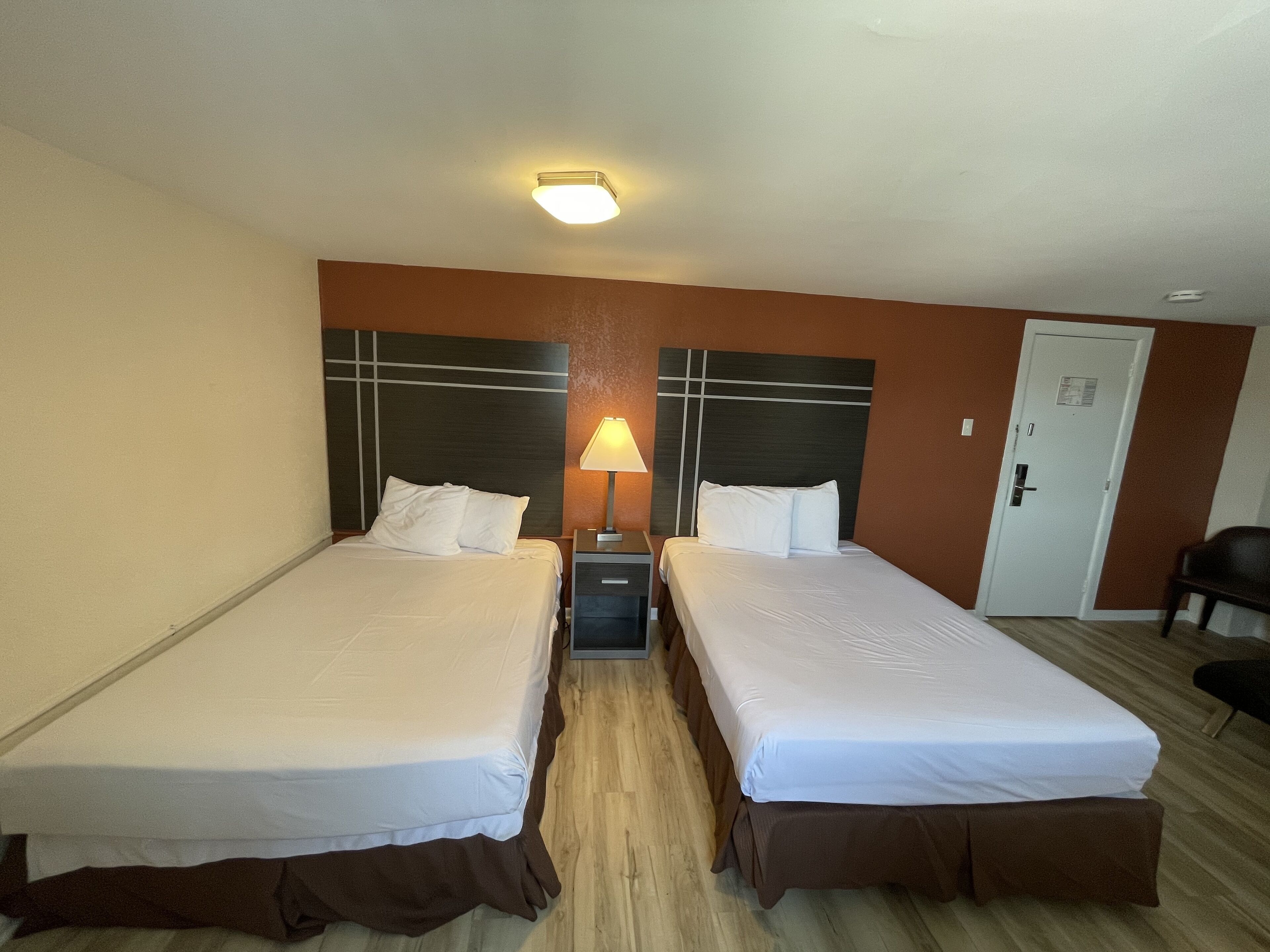 Et hotelværelse med to senge, et sengebord, en lampe og en dør.