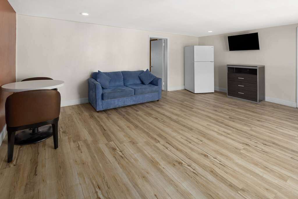 Une pièce moderne et minimaliste, avec un plancher en bois, un canapé bleu, une petite table ronde, un réfrigérateur blanc et un téléviseur fixé au mur.