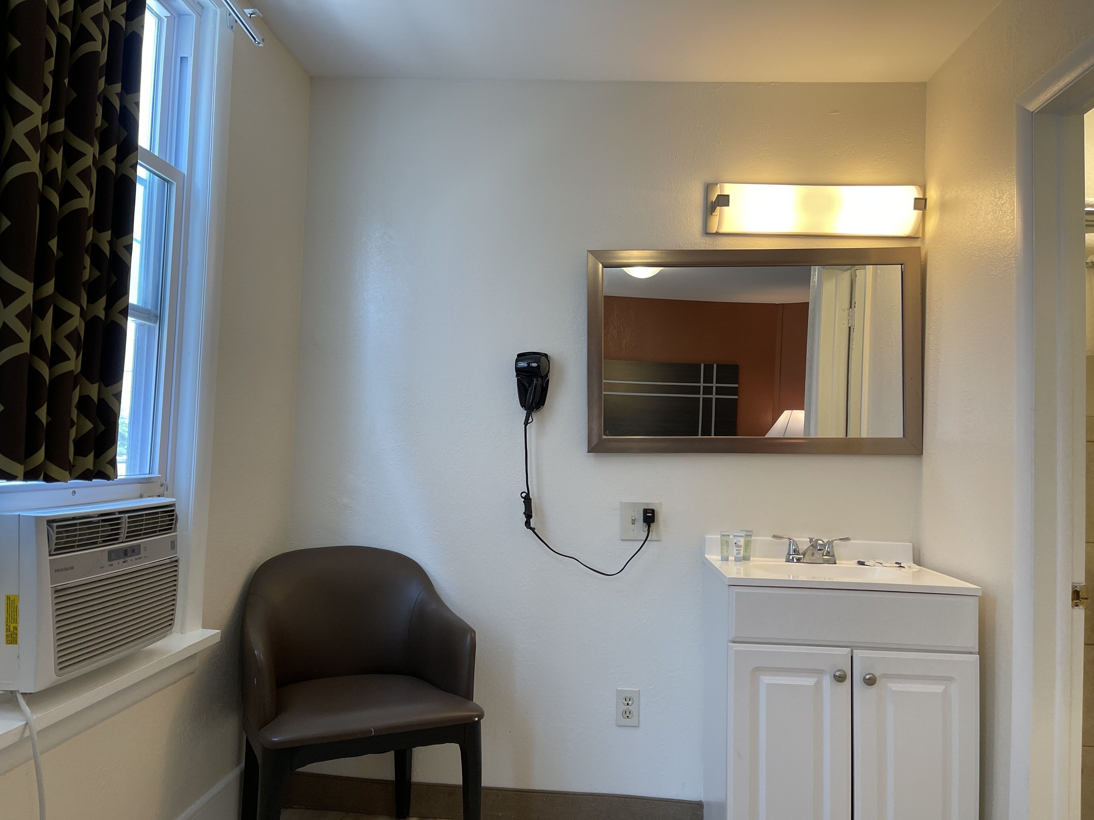 Une salle de bain équipée d’une chaise, d’un lavabo, d’un miroir et d’un appareil de climatisation.