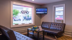 A modern lobby with a leather sofa, a small table with a bowl of fruit, and a TV mounted on the wall.