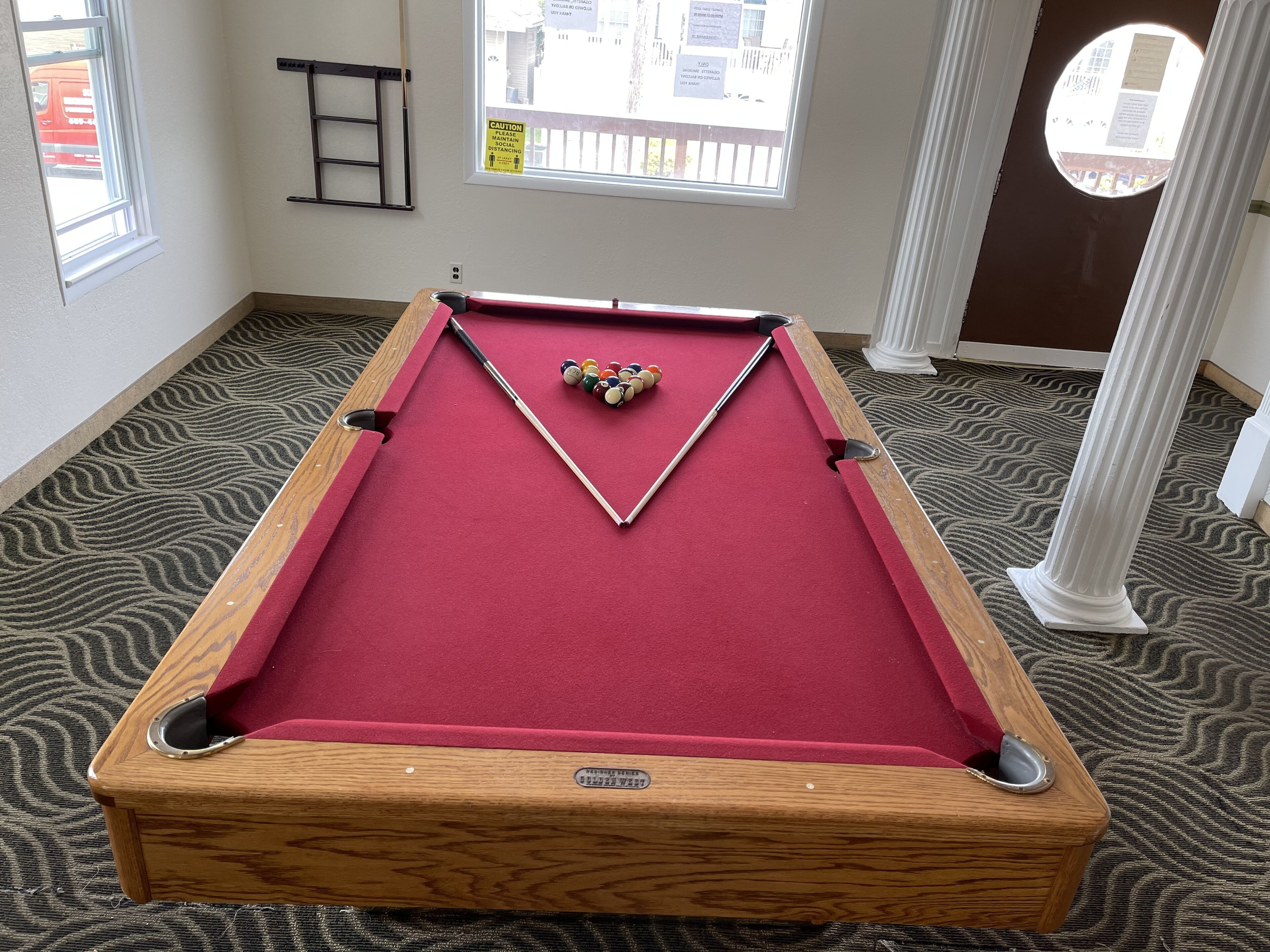A pool table with balls and cues, a wooden side table, a ladder, and a patterned carpet.