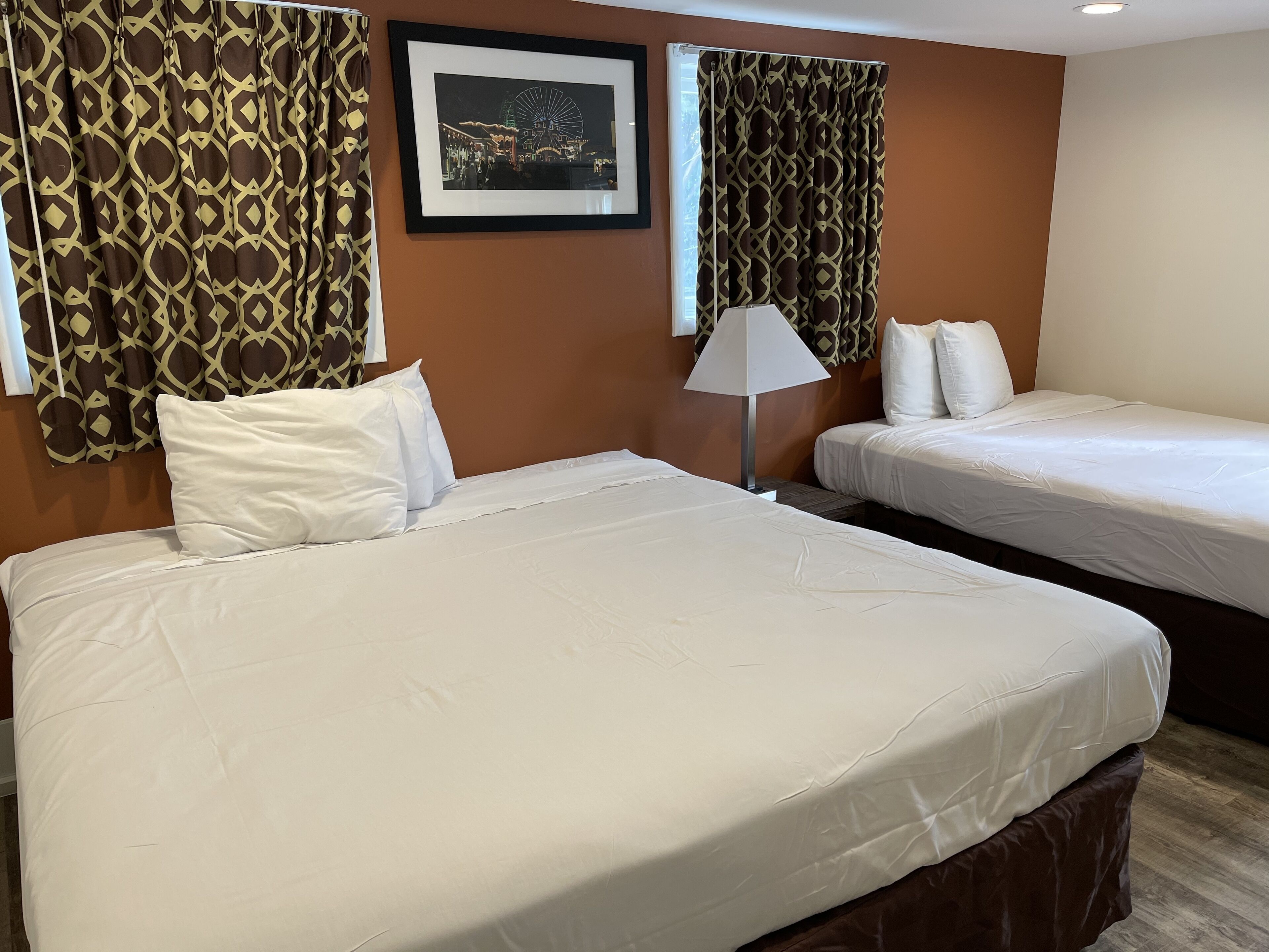 A hotel room with two beds, a framed picture on the wall, and patterned curtains.