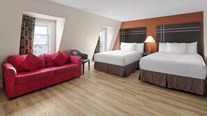 A hotel room with two beds, a red sofa, and a wooden floor.