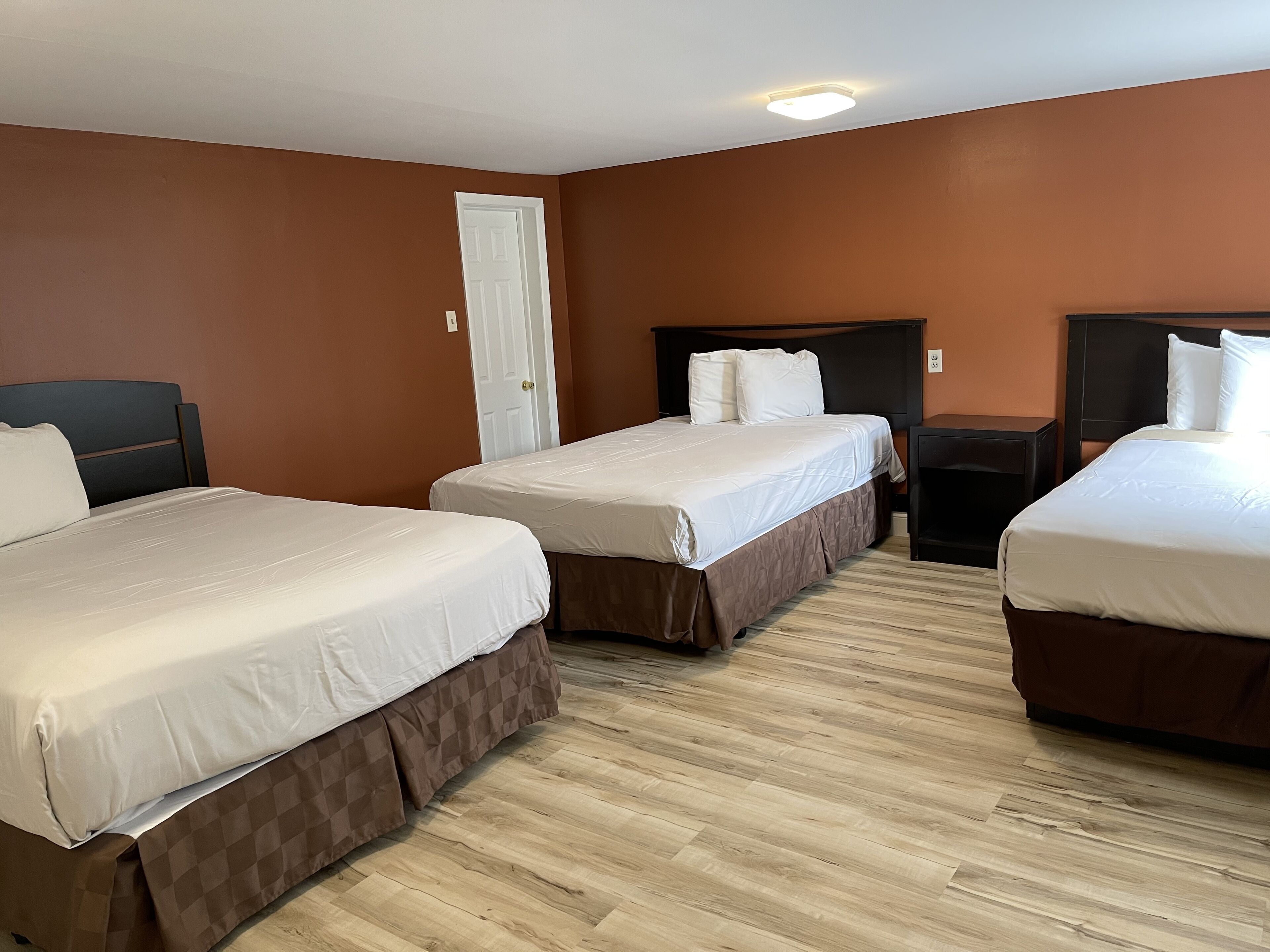 A hotel room with two beds, a wooden floor, and a white door.