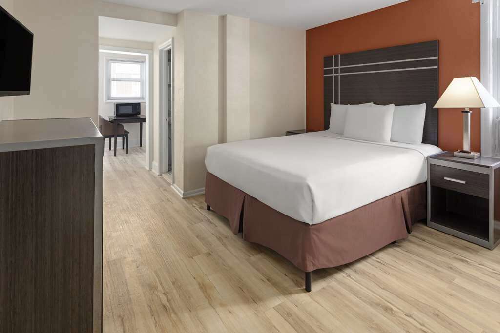 Una habitación de hotel con una cama grande, un escritorio con silla y un televisor en la pared.