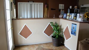 A reception area with a counter, framed bulletin boards, a potted plant, and a window with curtains. - Savannah Motel (Savannah)