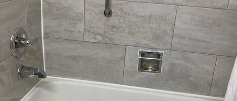 A bathtub with a handheld showerhead, a towel, and a wall-mounted faucet.