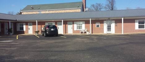 A building with a parking lot, a black car parked in the lot, and a sign that reads "OFFICE".