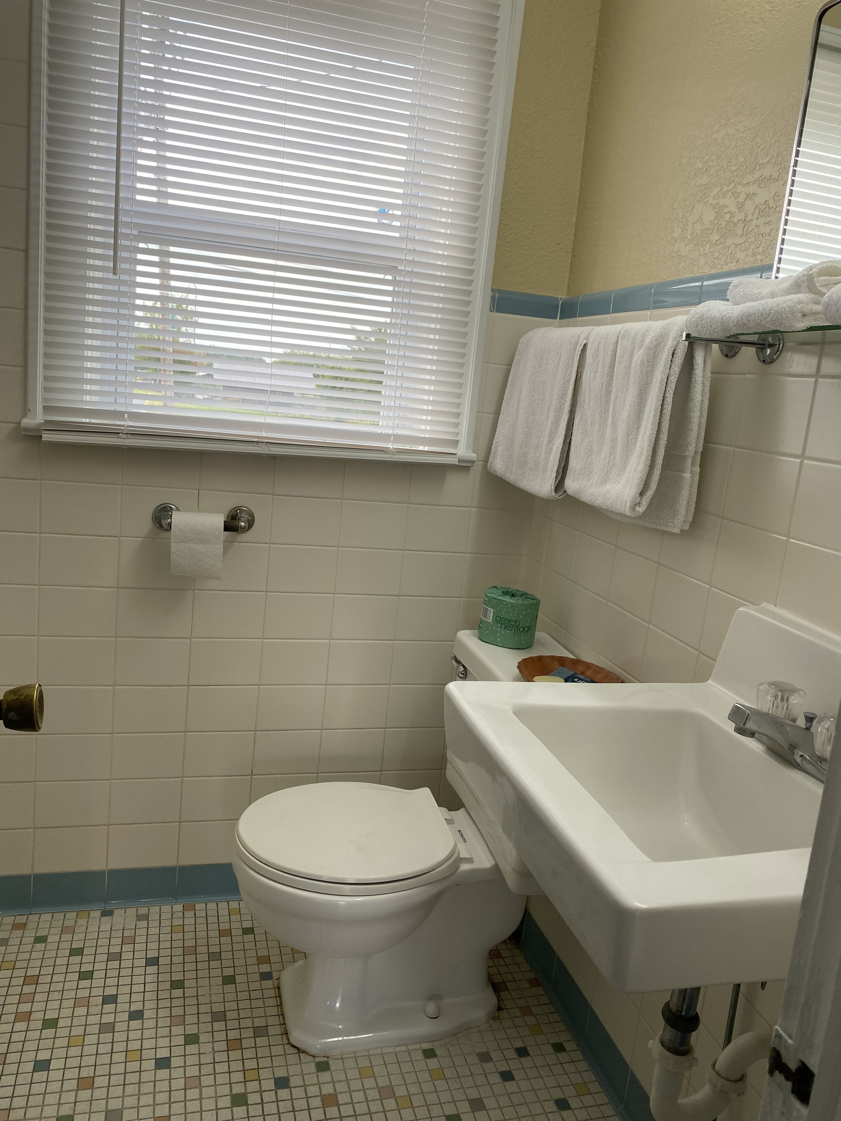 A bathroom with a toilet, a bathtub, and a window with blinds.