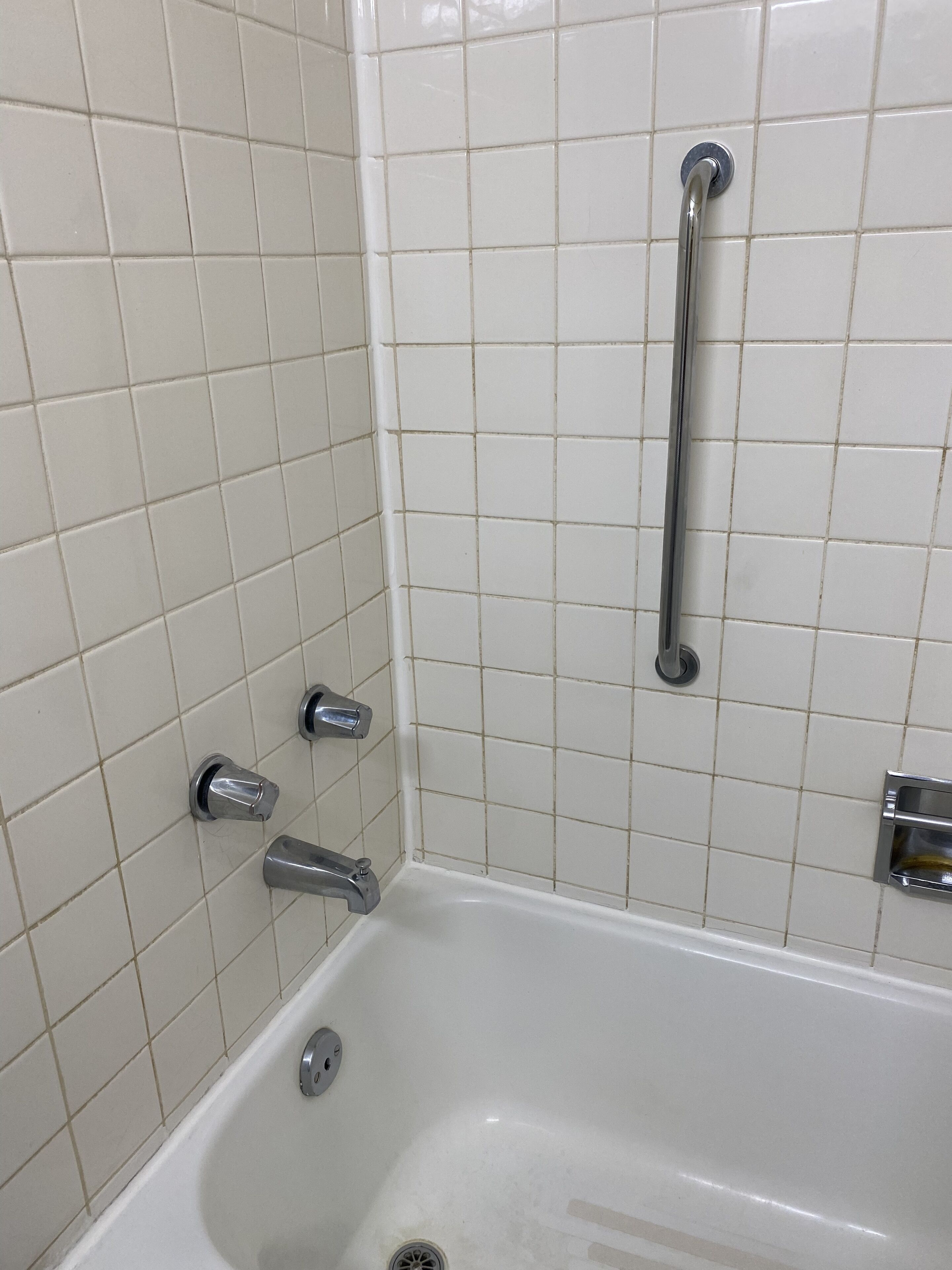Un baño con revestimiento blanco, una bañera, un cabezal de ducha y una barra de apoyo.