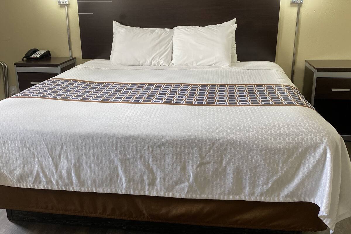 A hotel room with a large bed, two bedside tables, a phone on one table, and two wall-mounted lamps.