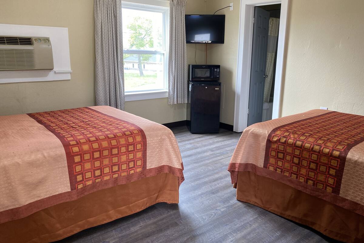 A hotel room with two beds, a television, a refrigerator, and a window with curtains.