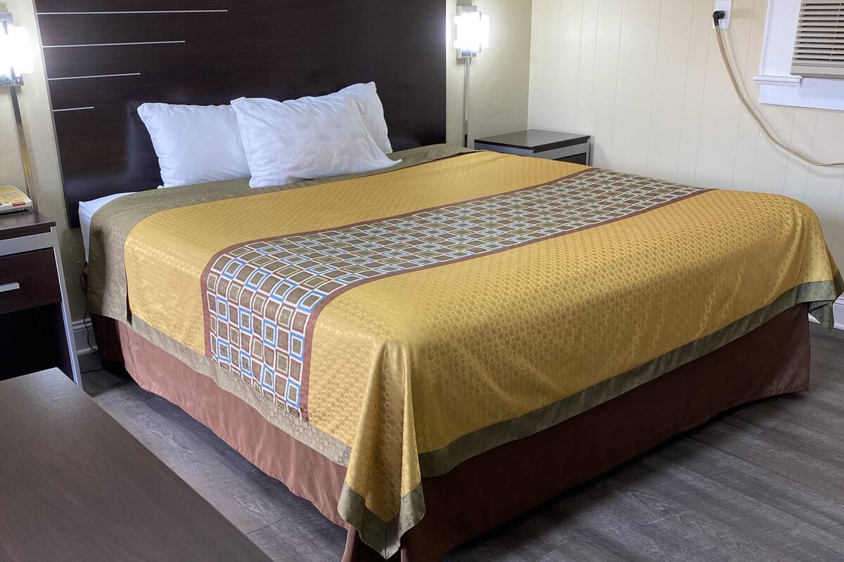 A neatly made bed with a patterned bedspread, a bedside table with a lamp, and a wooden nightstand.
