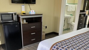 A hotel room with a bed, a desk with a microwave, a TV, and a bathroom visible through an open door. - Savannah Motel (Savannah)