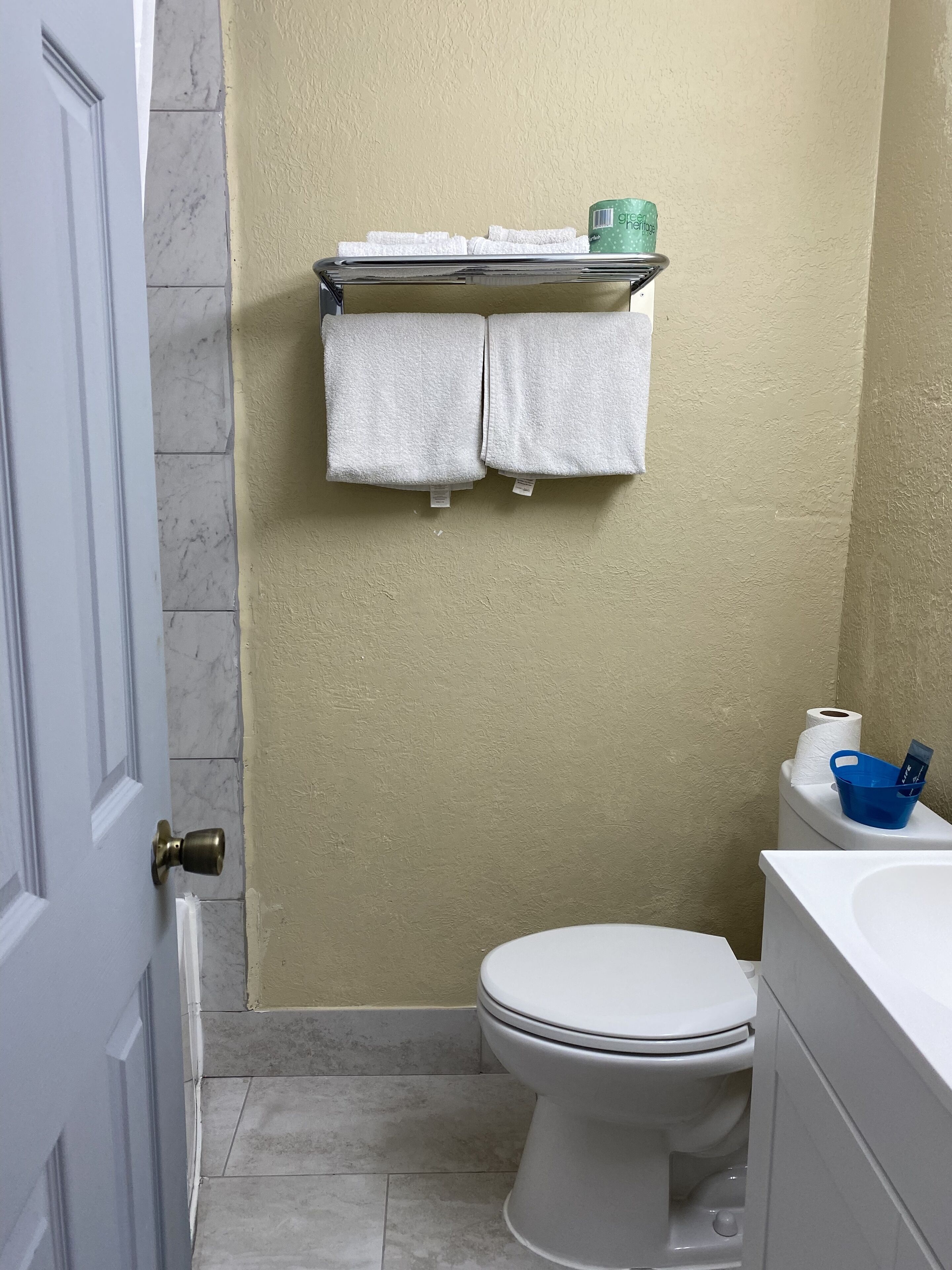 Een badkamer met een toilet, een plank met handdoeken, een blauwe mand en een toiletrol.