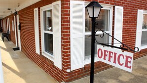 A brick building with white shutters, a sign reading "OFFICE", and a black lamp post. - Savannah Motel (Savannah)