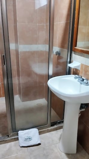 Un baño con cabina de ducha de vidrio, un lavamanos blanco y una toalla en el suelo.