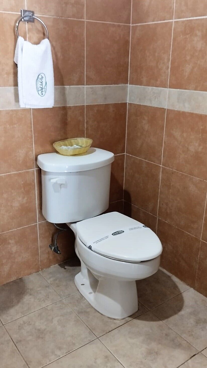 Casa de banho com sanita, uma cesta sobre o autoclismo e uma toalha pendurada num suporte de metal.