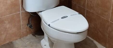 A bathroom with a toilet, a basket on the tank, and a towel hanging on a metal ring.