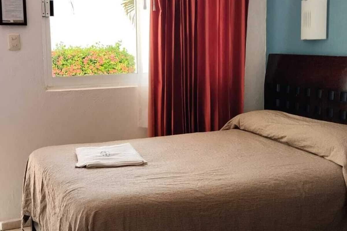 A room with two beds, a ceiling fan, a window with curtains, and a blue wall.